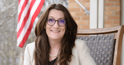 State Senator Veronica Klinefelt sits in a chair on a porch with an American flag behind her.