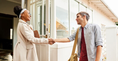 Two people shake hands outside of a home while conducting campaign canvassing.