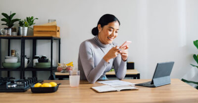 An organizer looking at their phone sits at a kitchen table with their laptop using a political text messaging service.