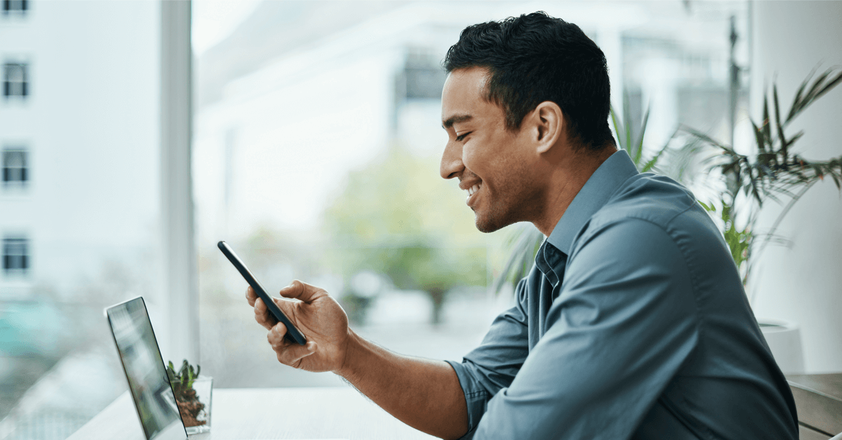 A smiling political staffer looks at their phone and computer while using digital tools for political campaigns.