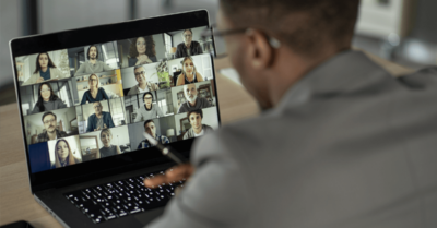 A political candidate speaking to a screen showing attendees at a virtual event.