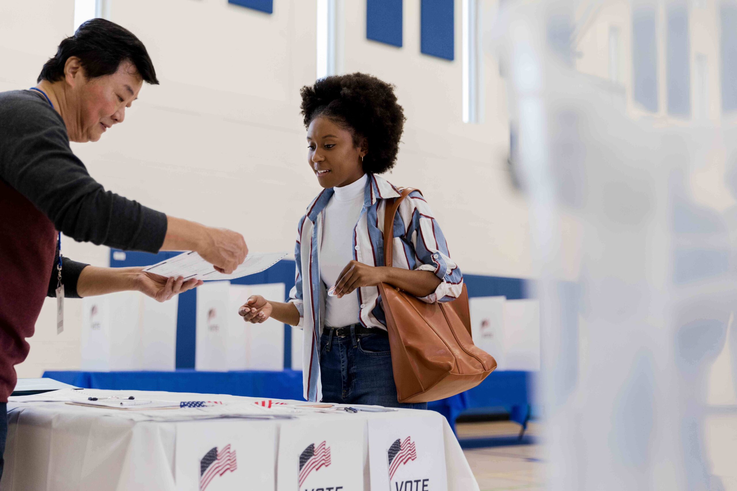 A man standing behind a table hands a woman a piece of paper describing how to get on the ballot.