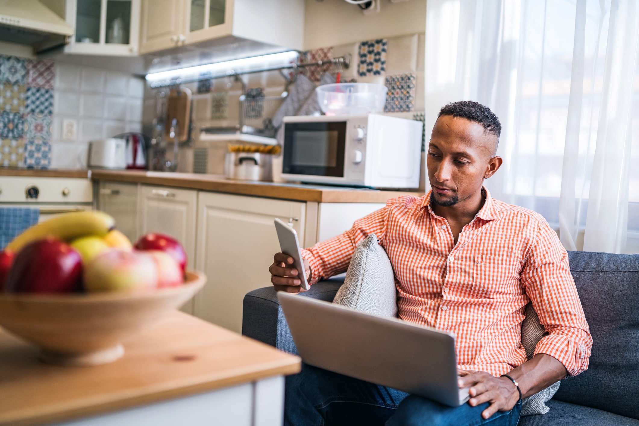 A man holding a cell phone and a laptop participates in phone canvassing from his kitchen at home.