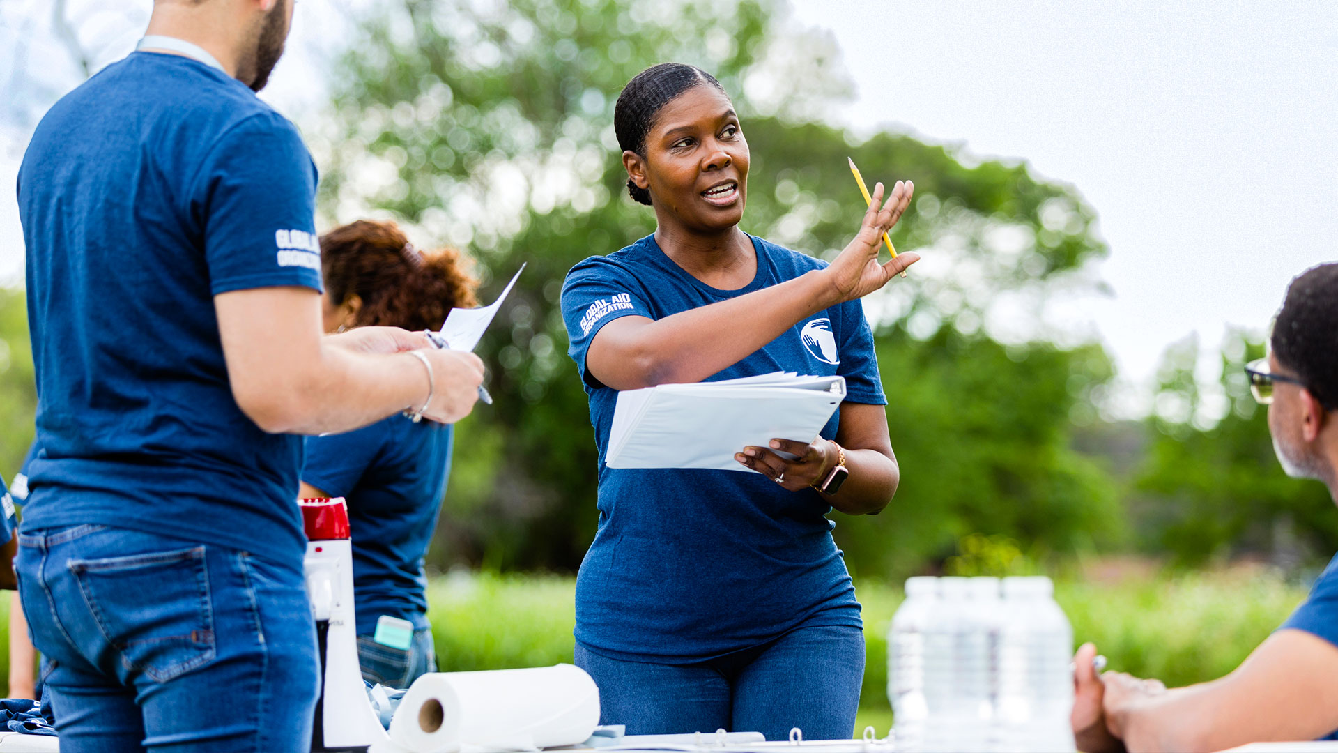 A diverse group of nonprofit volunteers in navy shirts gather outdoors, smiling and coordinating activities.