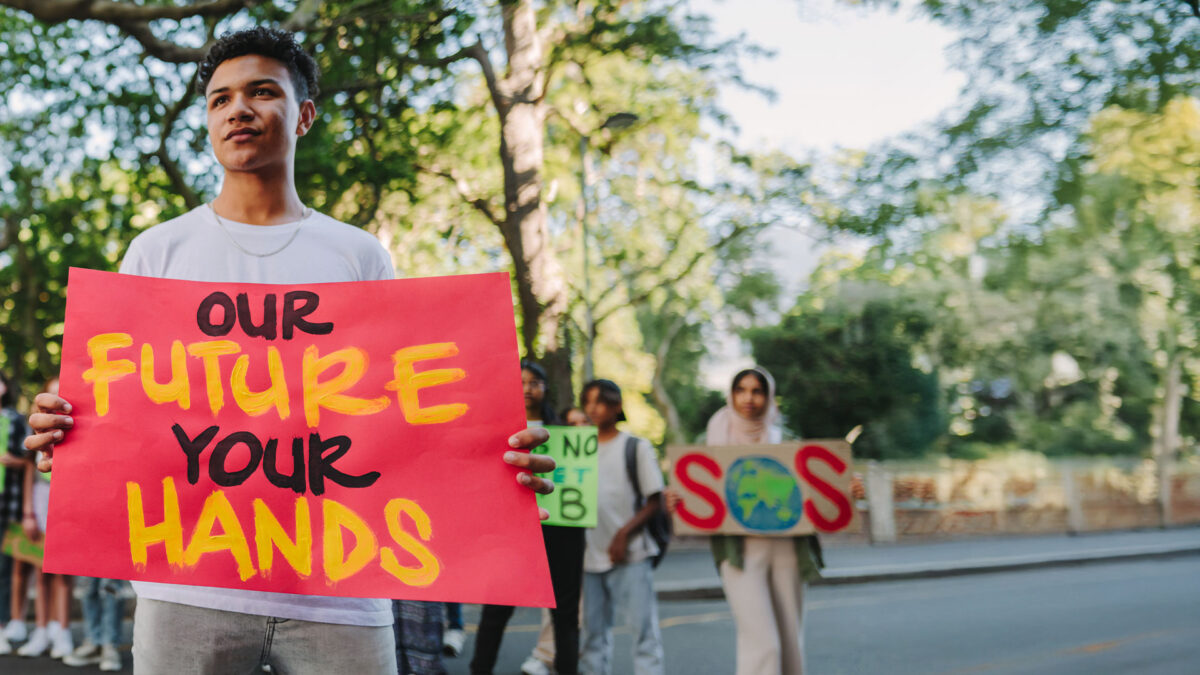 A young activist holds a bright protest sign reading ‘Our Future Your Hands’ at a community demonstration.