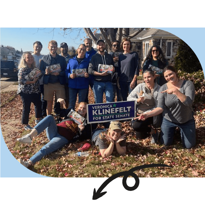 A group of volunteers gathered around a "Veronica Klinefelt for State Senate" yard sign in a neighborhood.