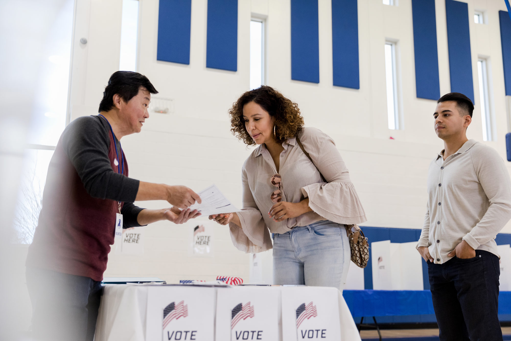 Three people at a polling location in a gym