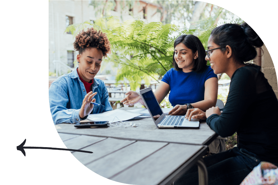 Three people seated at a table — one on a laptop, one with a pen and paper, and another between them pointing at the notebook